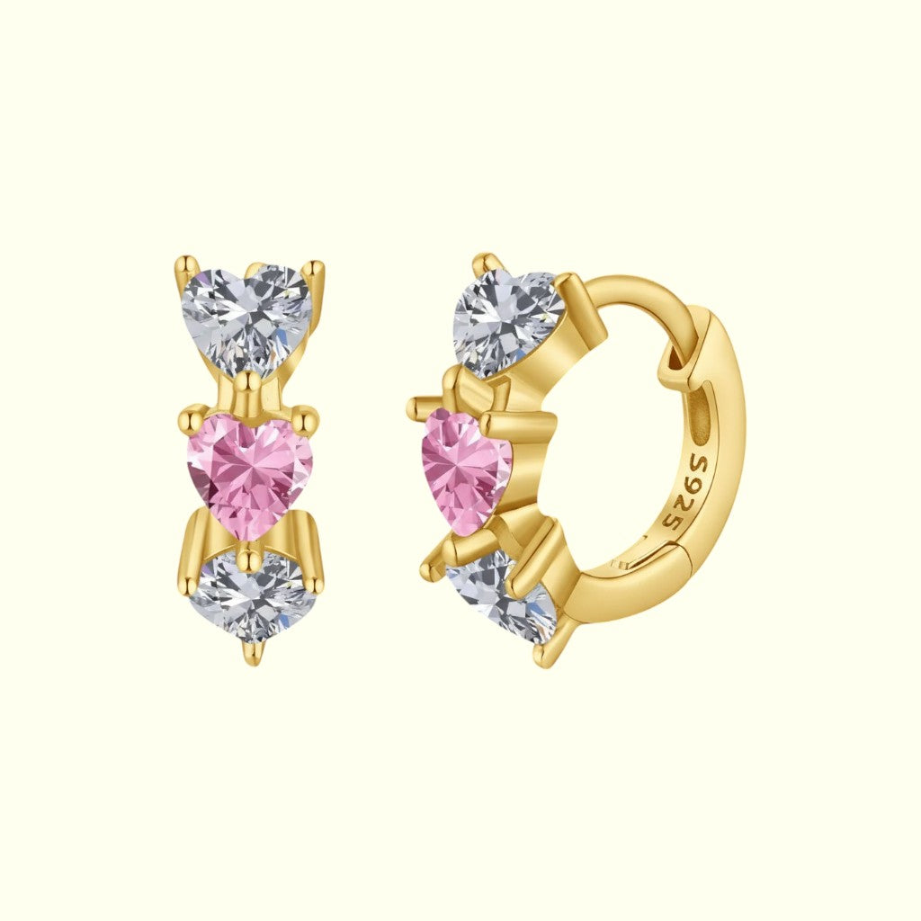 Gold hoop earrings with heart-shaped pink and clear gemstones on a white background