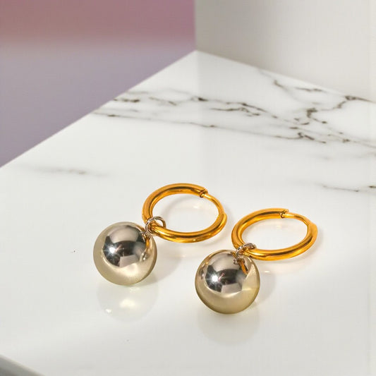 Gold hoop earrings with silver spherical charms on a marble surface