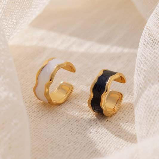 Gold and black open-style earrings on a textured beige surface