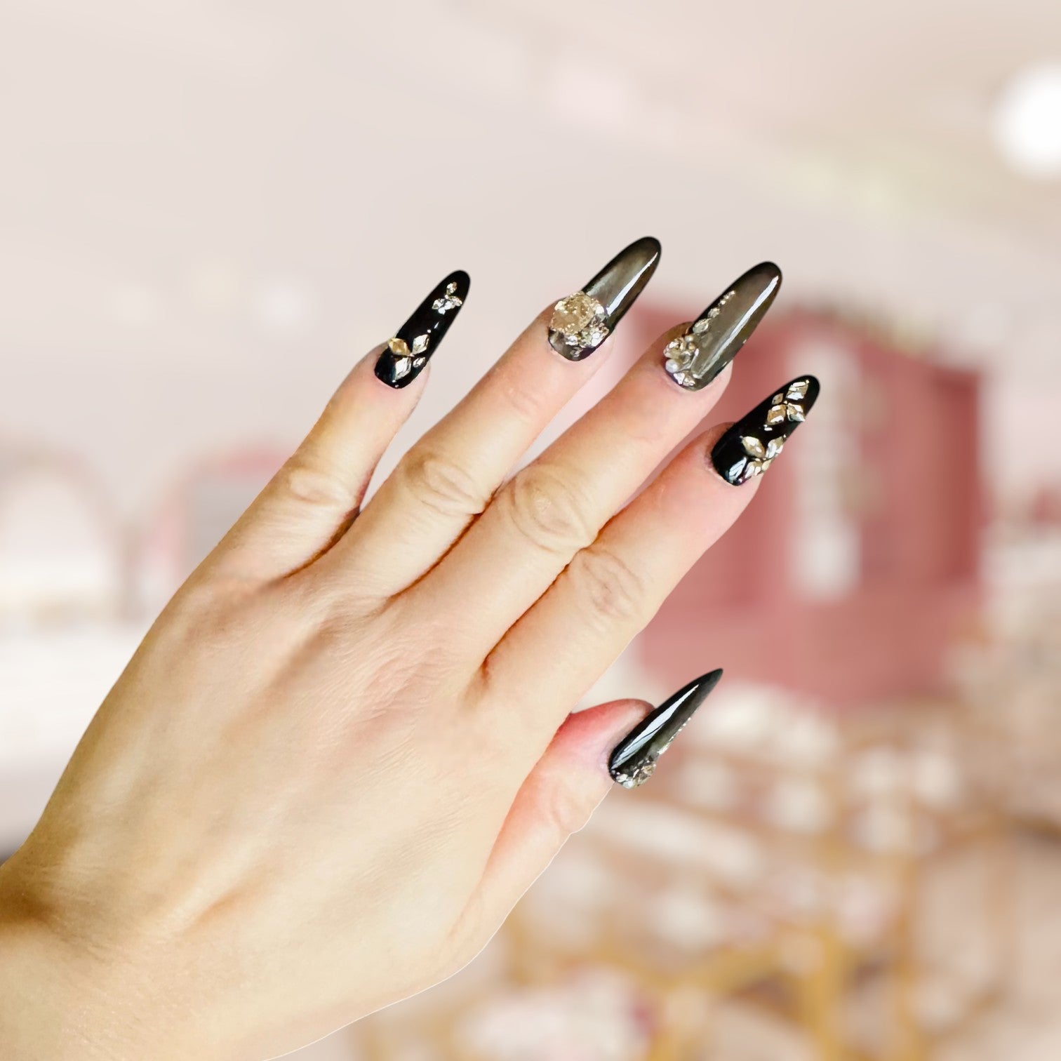 Hand with black nail art featuring gold decorations against a blurred background