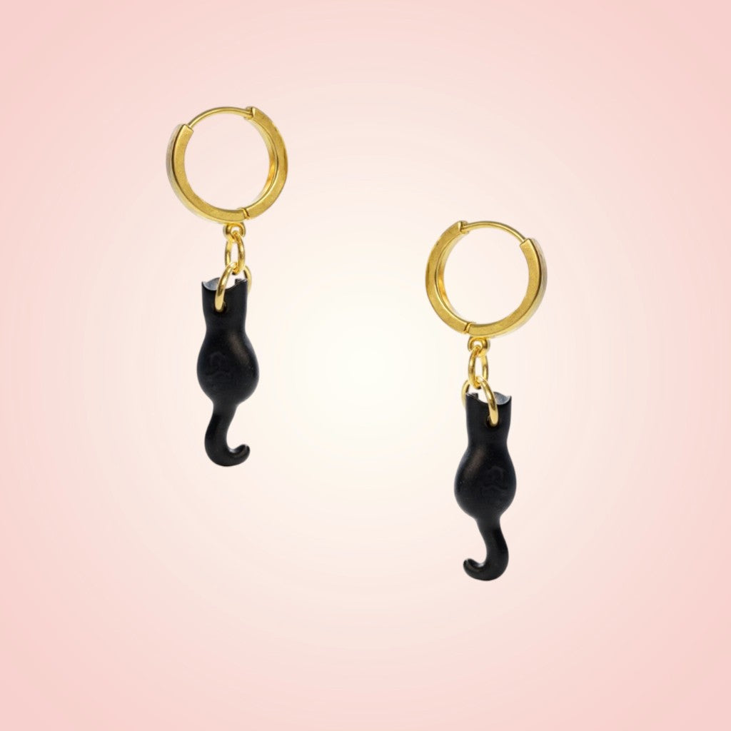 Gold hoop earrings with black cat-shaped charms on a pink background