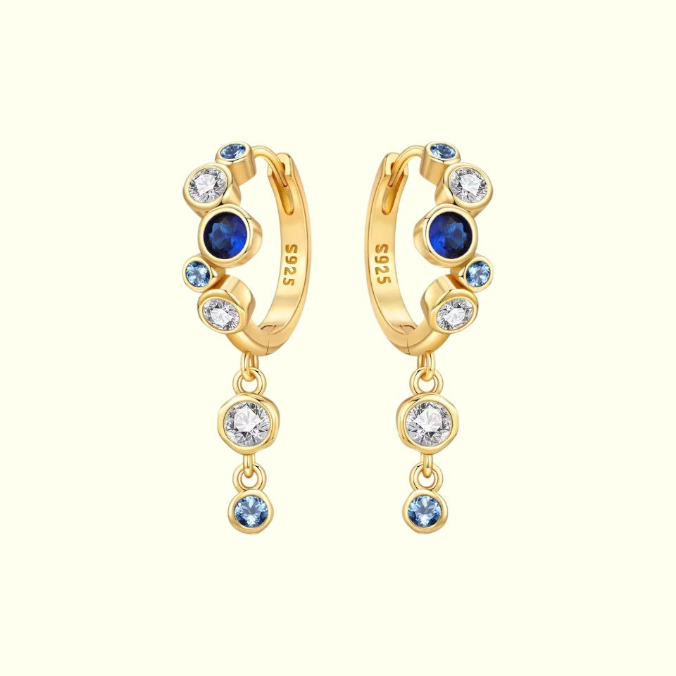 Gold hoop earrings with blue and clear gemstones on a white background