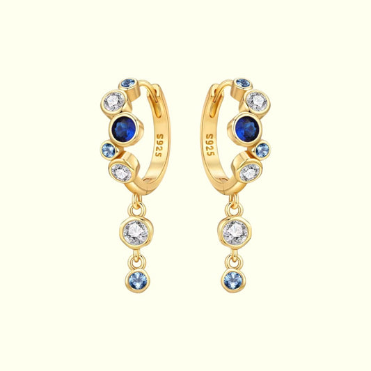 Gold hoop earrings with blue and clear gemstones on a white background