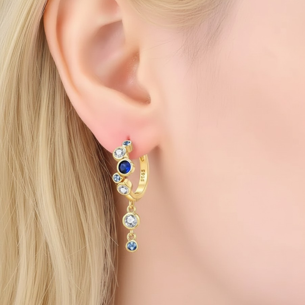Gold earring with blue gemstones worn by a person with blonde hair.