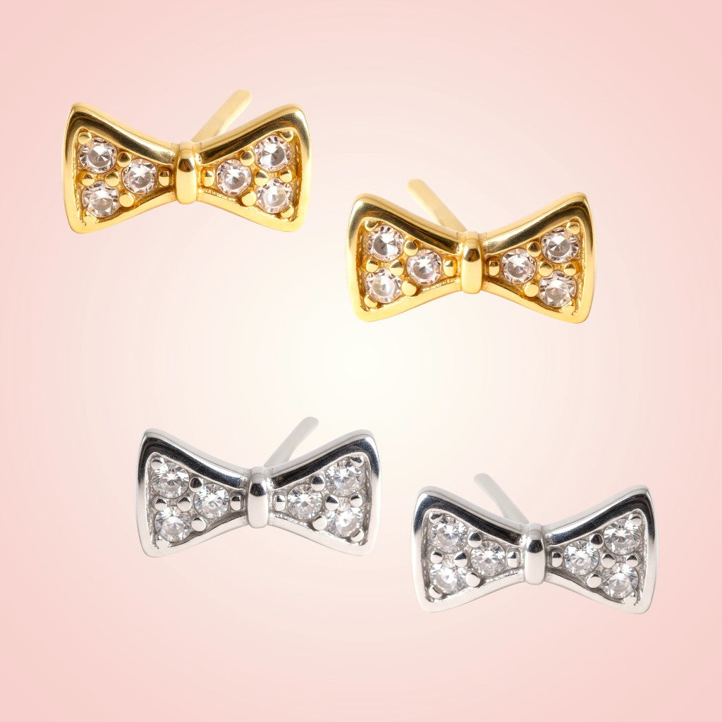 Bow-shaped earrings in gold and silver on a pink background