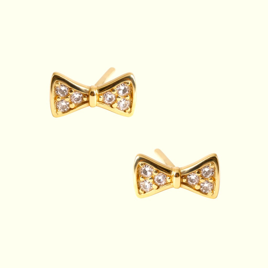 Gold bow-shaped earrings with clear gemstones on a white background