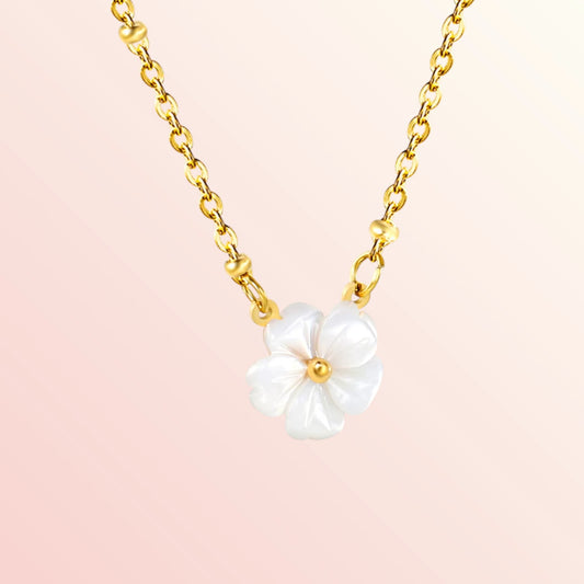 Gold necklace with a white floral pendant on a pink background