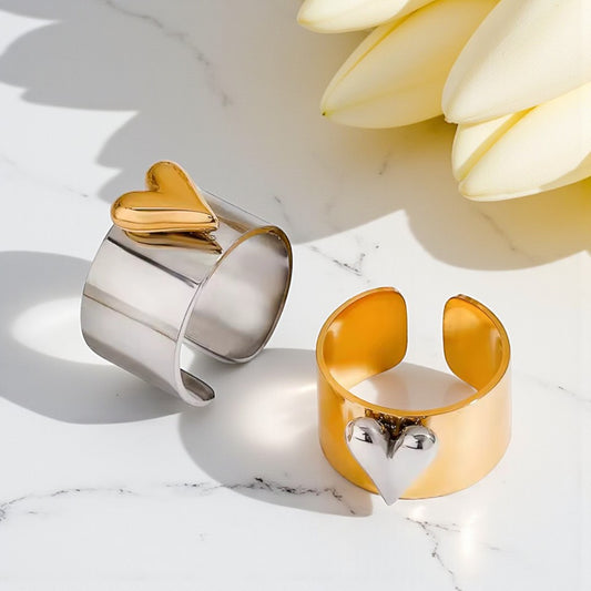 Two cuff rings, one gold and one silver, on a marble surface with a flower in the background.