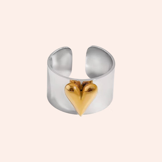 Silver ring with a gold heart-shaped accent on a light pink background