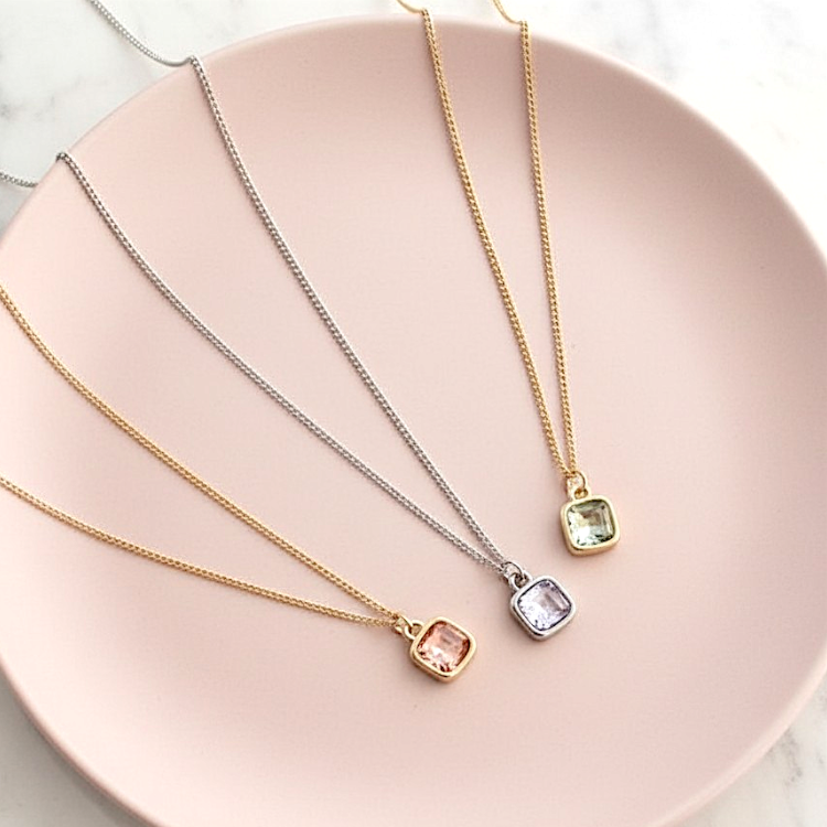 Three necklaces with square gemstones on a pink plate