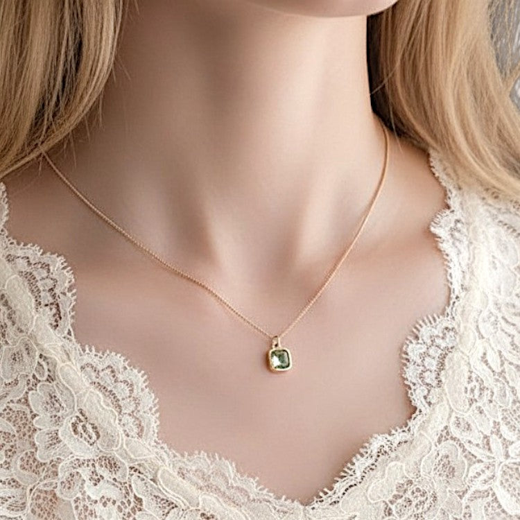 Gold necklace with a green gemstone pendant on a lace garment