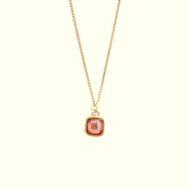 Gold necklace with a pink gemstone pendant on a beige background