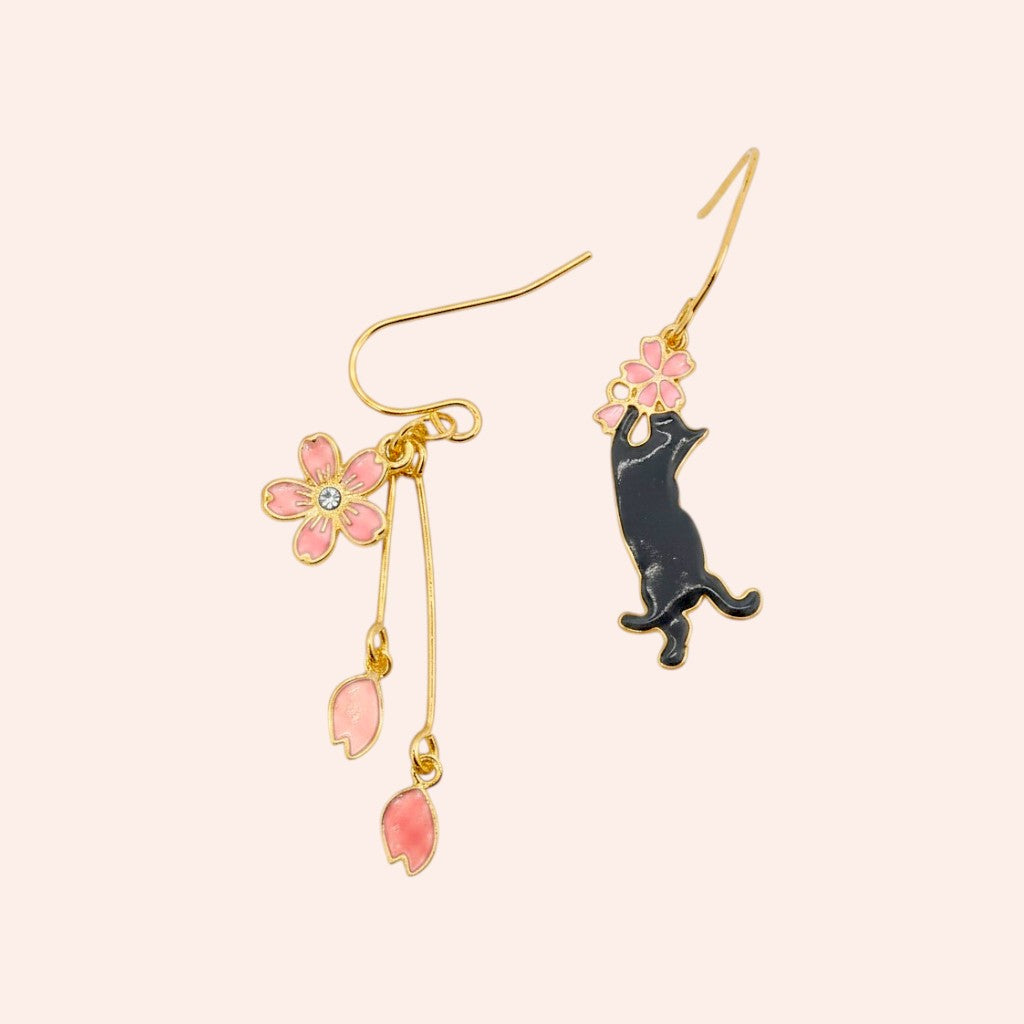 Earrings with a black cat and pink flower design on a light pink background