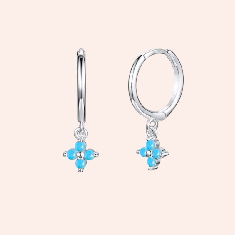 Silver hoop earrings with turquoise gemstones on a light pink background