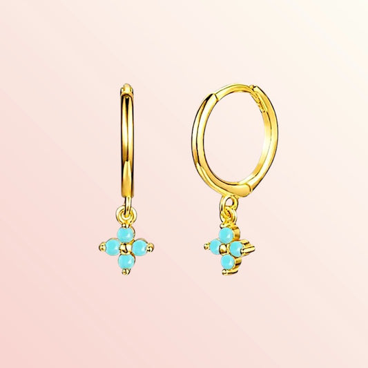 Gold hoop earrings with turquoise gemstones on a pink background