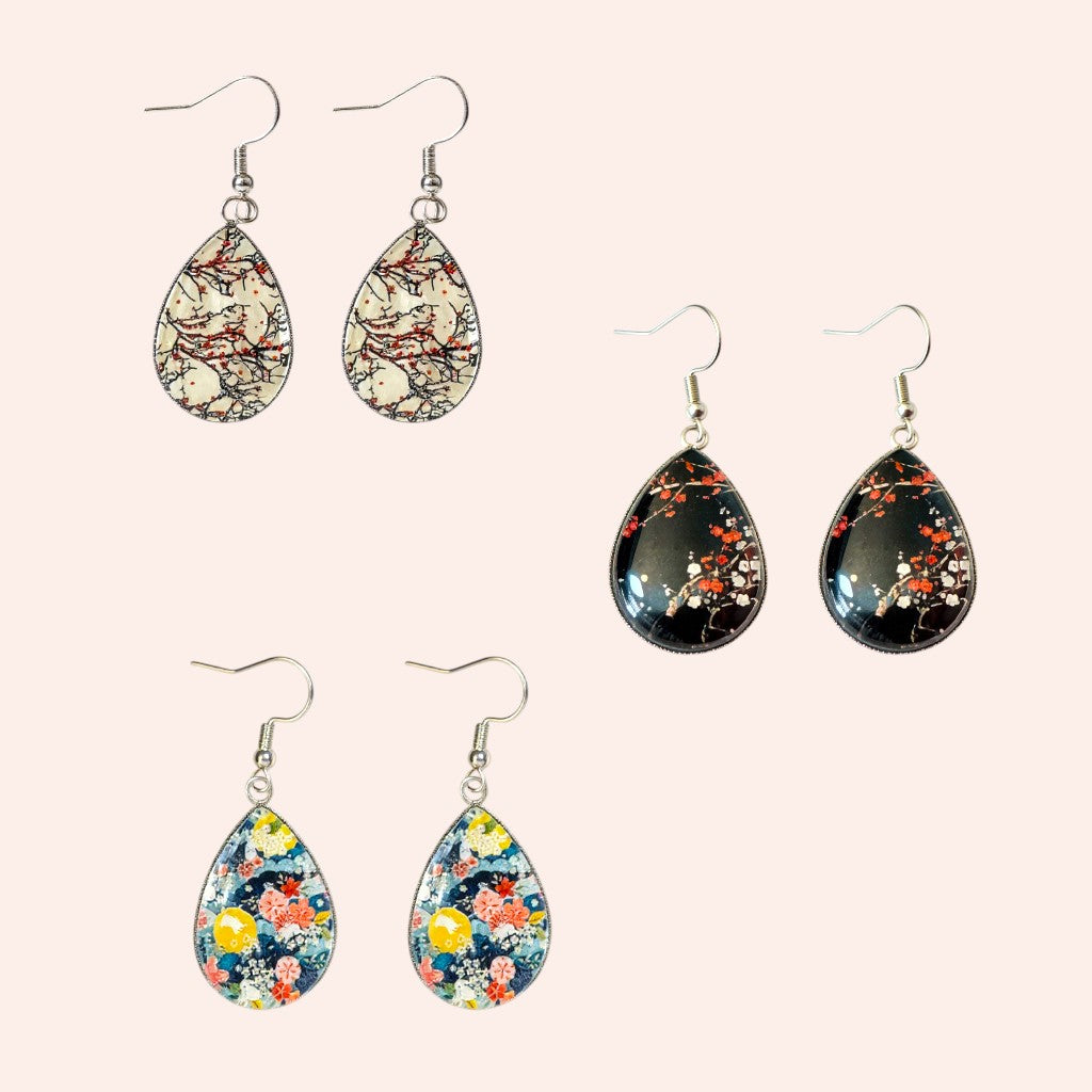 Set of teardrop-shaped earrings with floral patterns on a light pink background