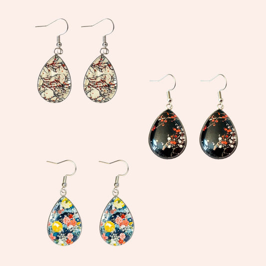 Set of teardrop-shaped earrings with floral patterns on a light pink background