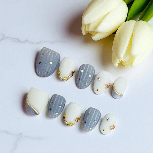 Decorative nail art with gold stars on nails next to white tulips on a marble background