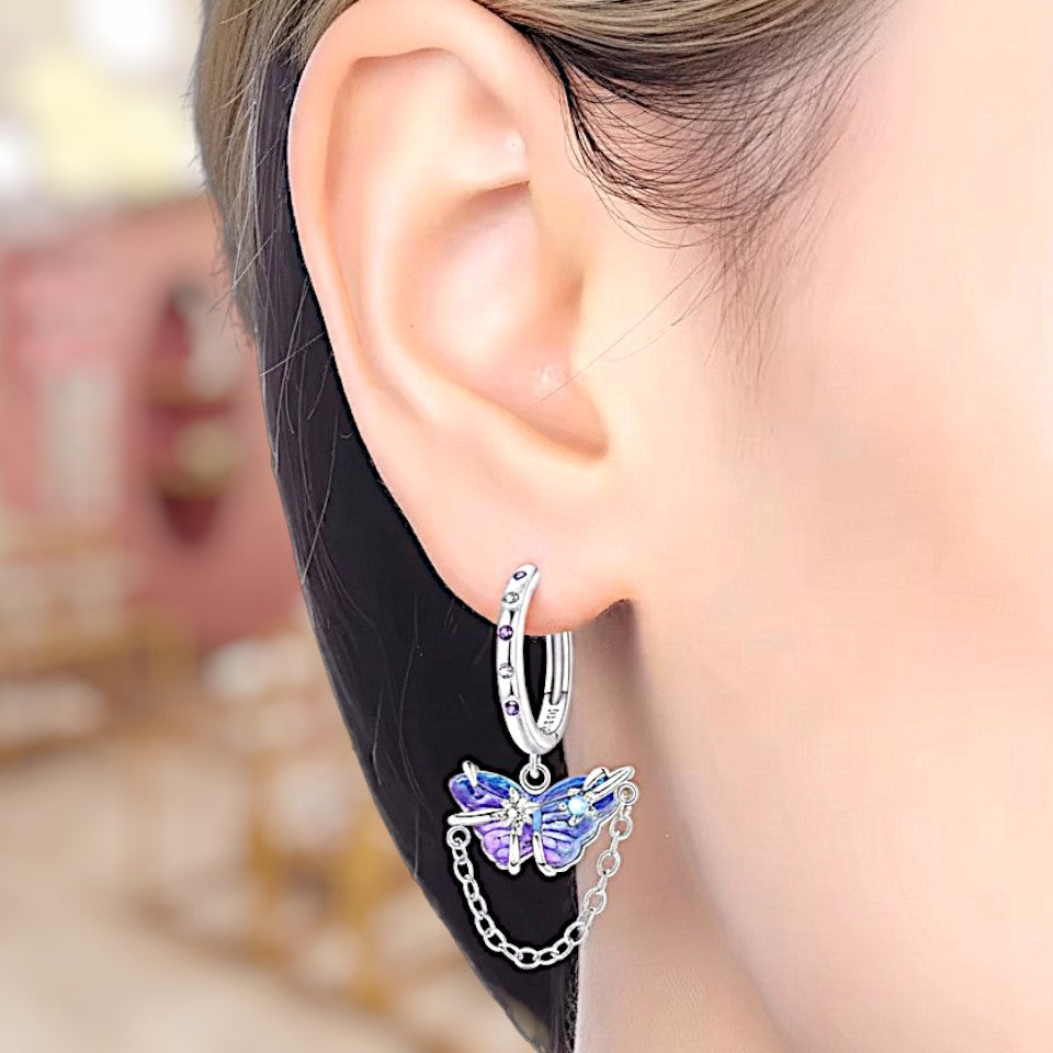 Silver hoop earring with a butterfly charm worn by a person.