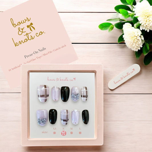 Set of press-on nails with decorative designs in a box on a wooden surface with flowers.