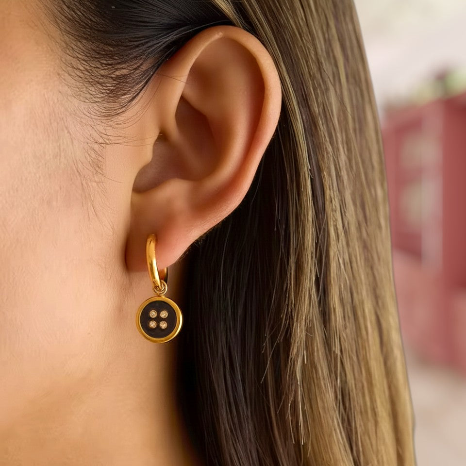 Close-up of a gold earring with a black stone worn by a person.