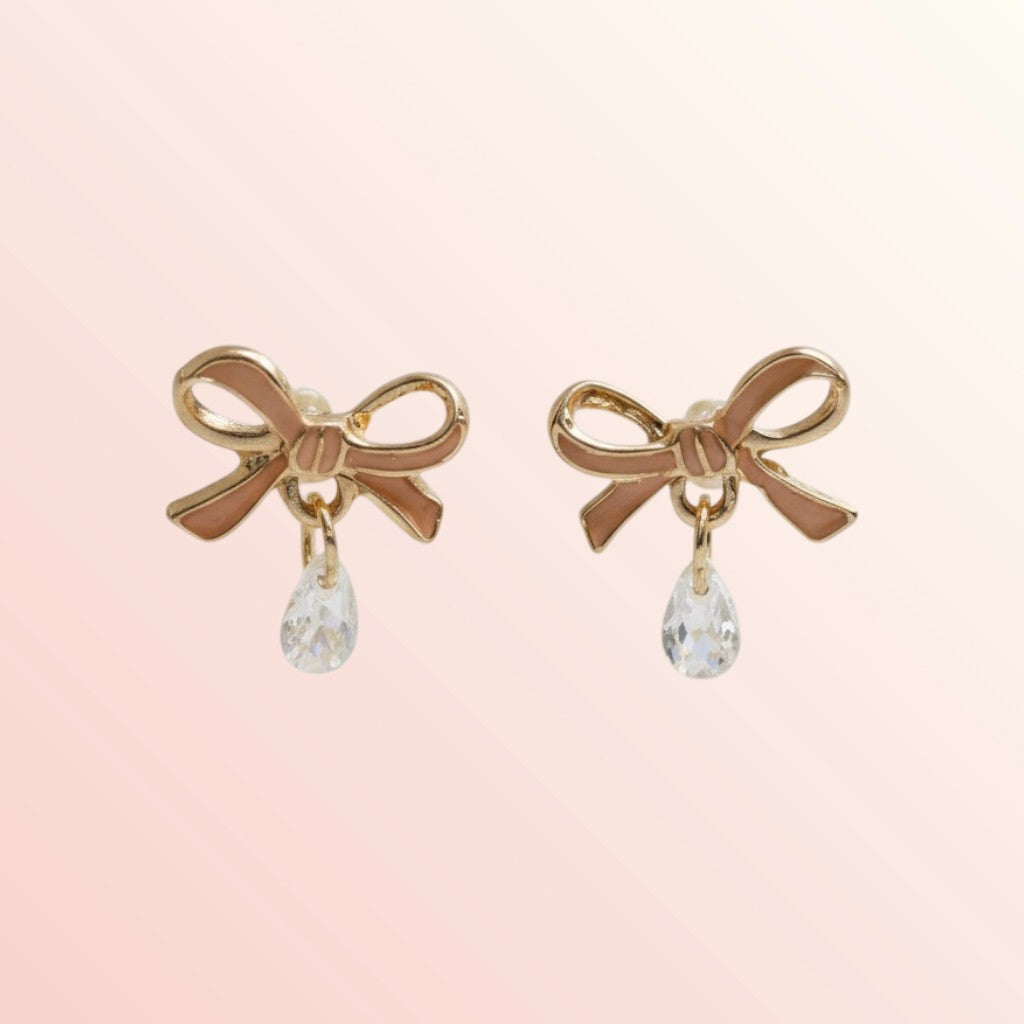 Gold bow-shaped earrings with clear teardrop charms on a pink background
