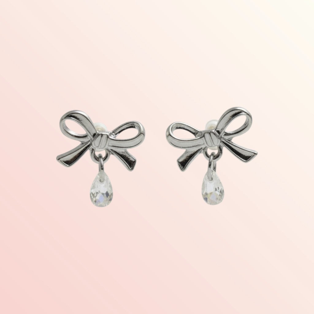 Silver bow-shaped earrings with teardrop charms on a light pink background