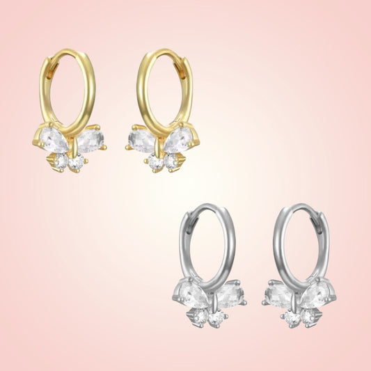 Gold and silver hoop earrings with butterfly-shaped gemstones on a pink background