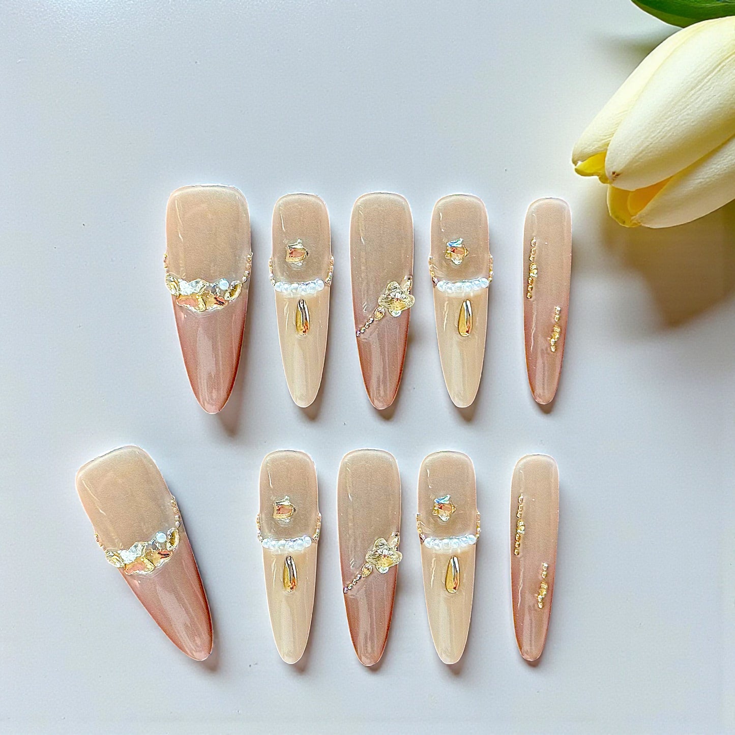 Set of decorative false nails with gold and silver accents on a white surface with a tulip.