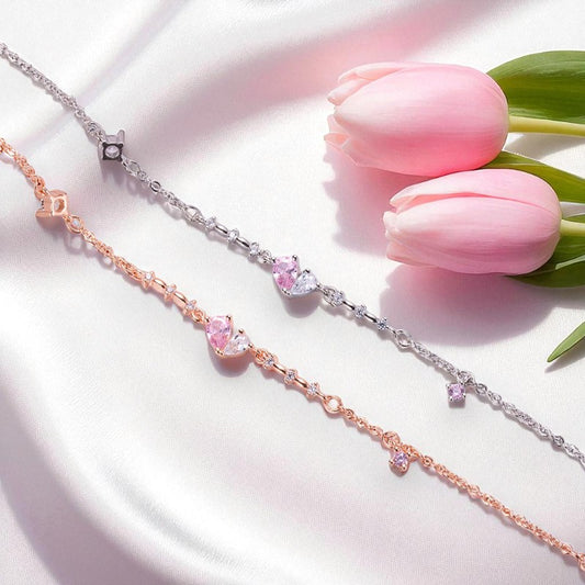 Two bracelets, one rose gold and one silver, with pink gemstones on a white surface with pink tulips.