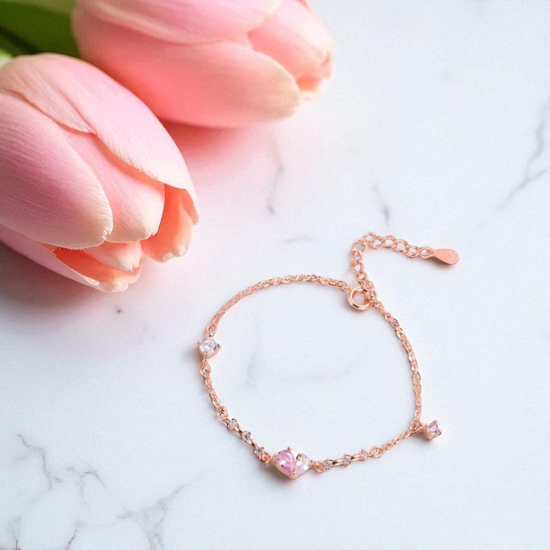 Rose gold bracelet with pink gemstones on a marble surface with pink tulips.