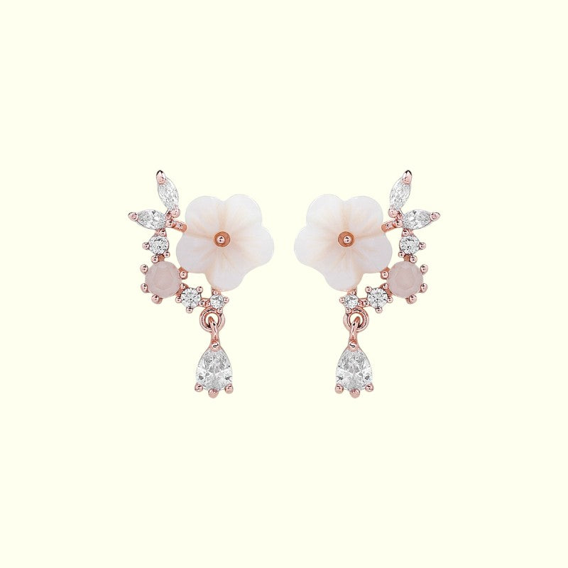 Pair of floral earrings with rose gold and clear gemstone accents on a white background