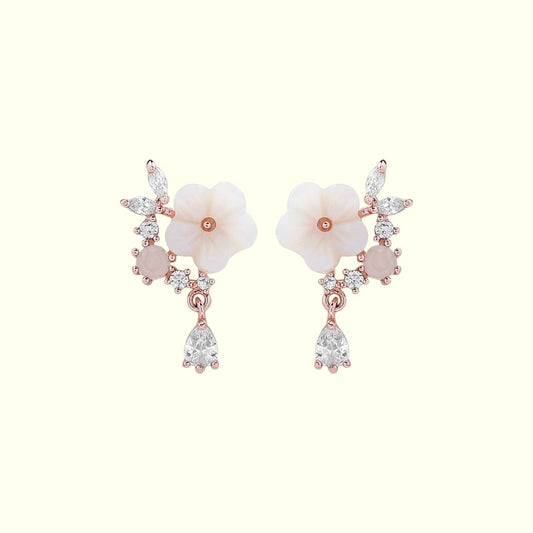 Pair of floral earrings with rose gold and clear gemstone accents on a white background