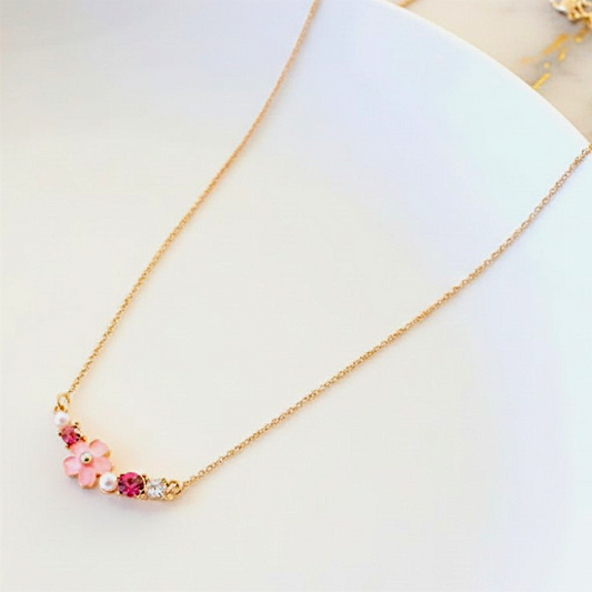 Delicate gold necklace with floral and berry-like pendants on a light background