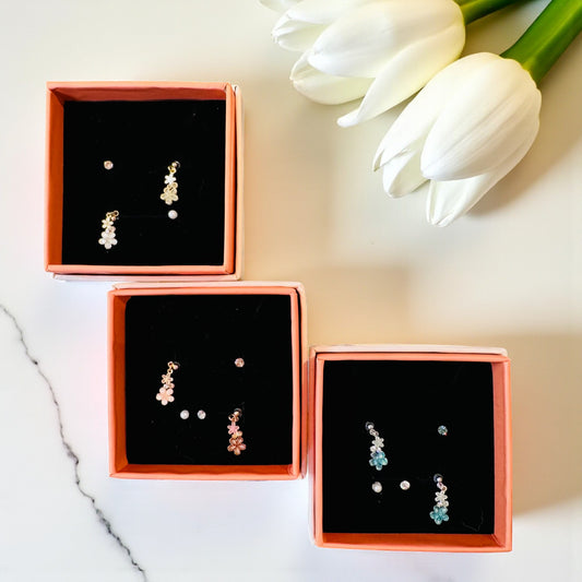 Three boxes of earrings on a marble surface with white tulips in the background
