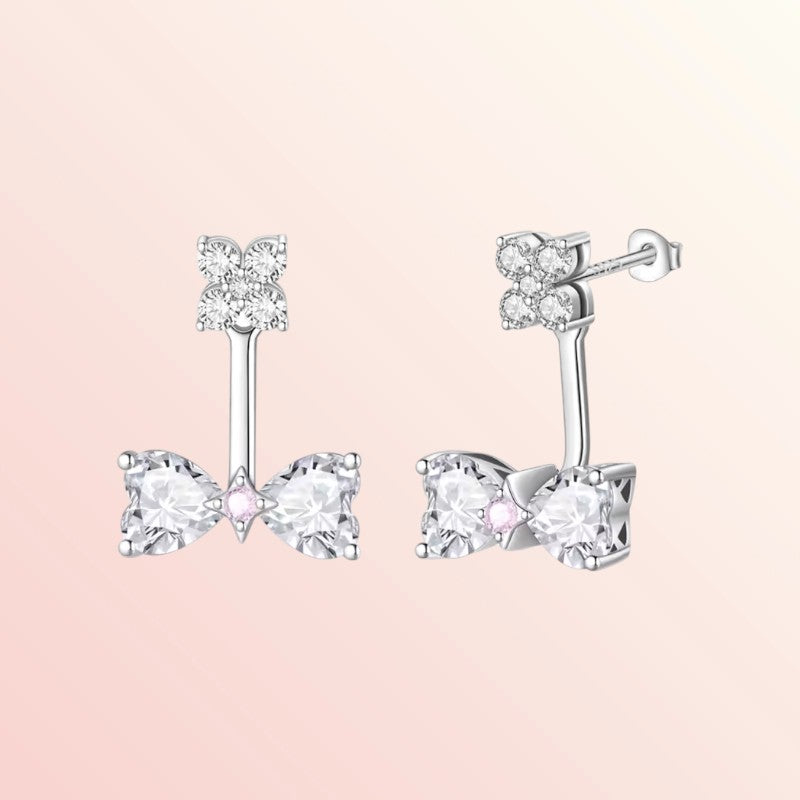 Bow-shaped silver earrings with clear gemstones on a light pink background