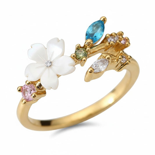 A gold-plated open ring featuring a white enamel flower with a clear center stone, a pink gemstone, a green gemstone, a blue marquise-cut gemstone, and clear marquise-cut gemstones, set against a plain white background.