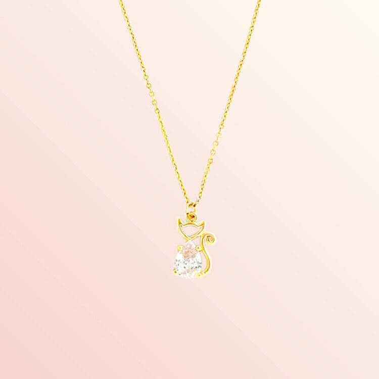 Gold cat-shaped necklace with a clear gemstone on a pink background