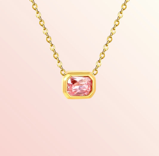 Gold necklace with a pink gemstone on a light pink background