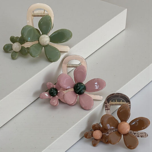 Three floral hair clips in green, pink, and brown on a white and gray background
