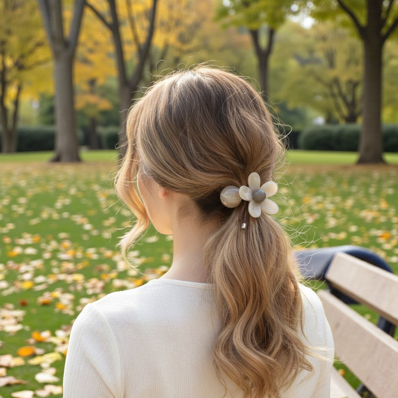 Person with a floral hair accessory in a park with trees and fallen leaves.