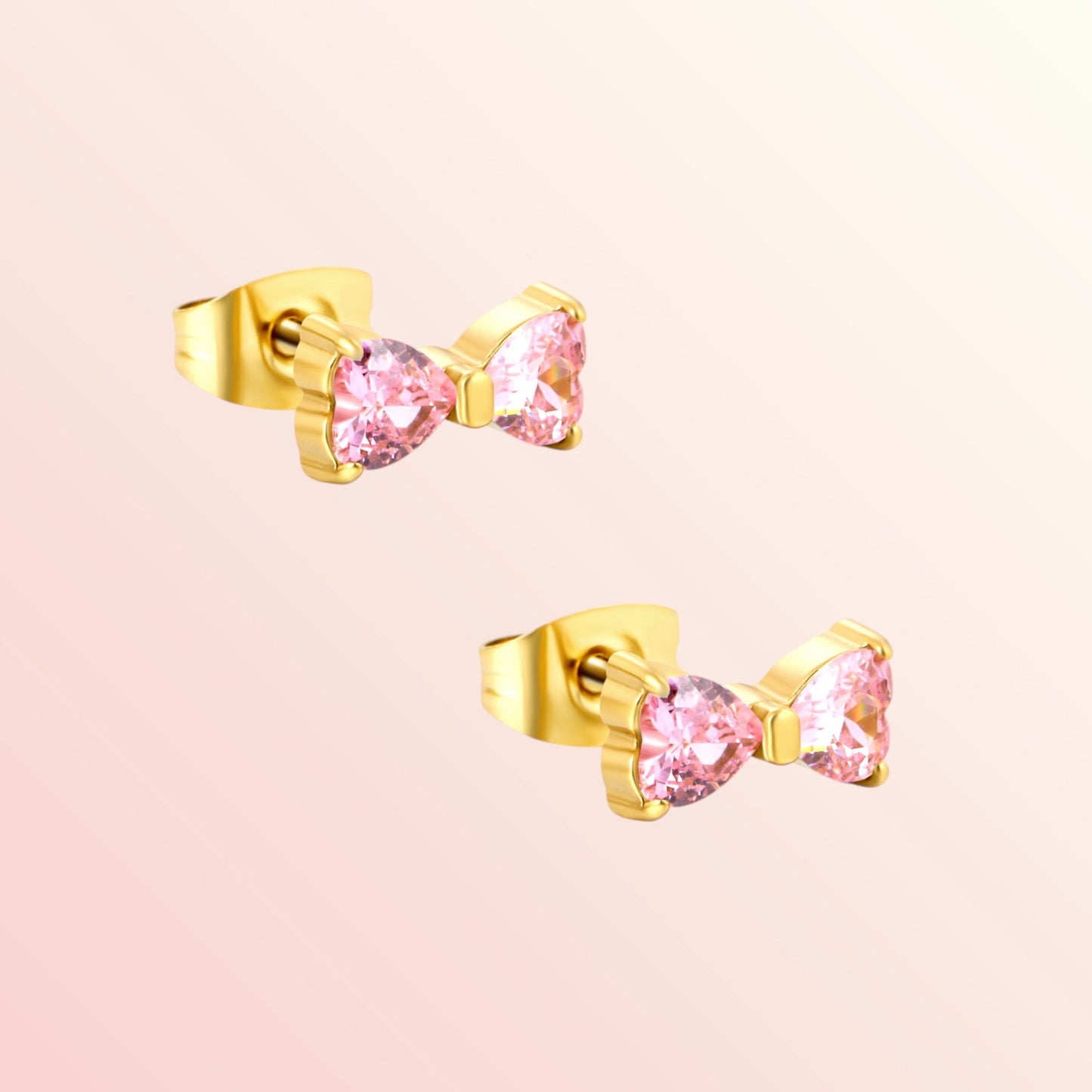 Gold bow-shaped earrings with pink gemstones on a light pink background