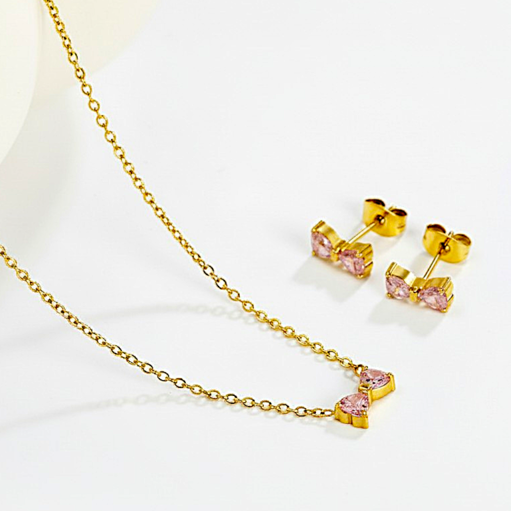 Gold necklace with pink heart-shaped stones and matching earrings on a white background