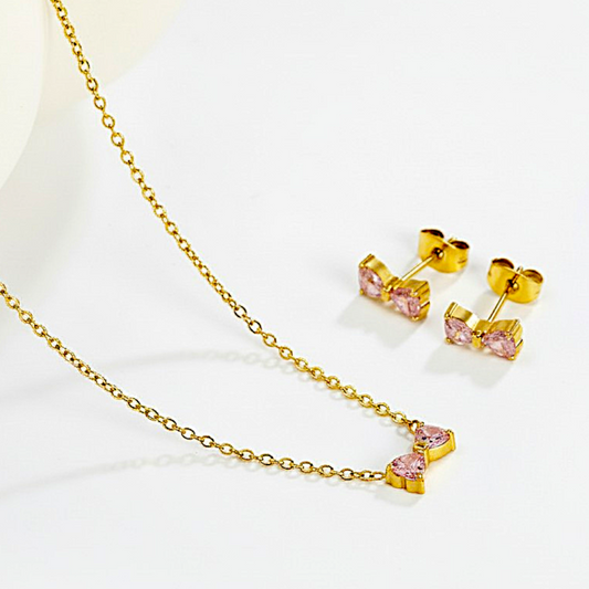 Gold necklace with pink heart-shaped stones and matching earrings on a white background