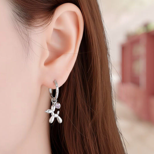 Silver earring with balloon dog charm worn by a person with long brown hair.