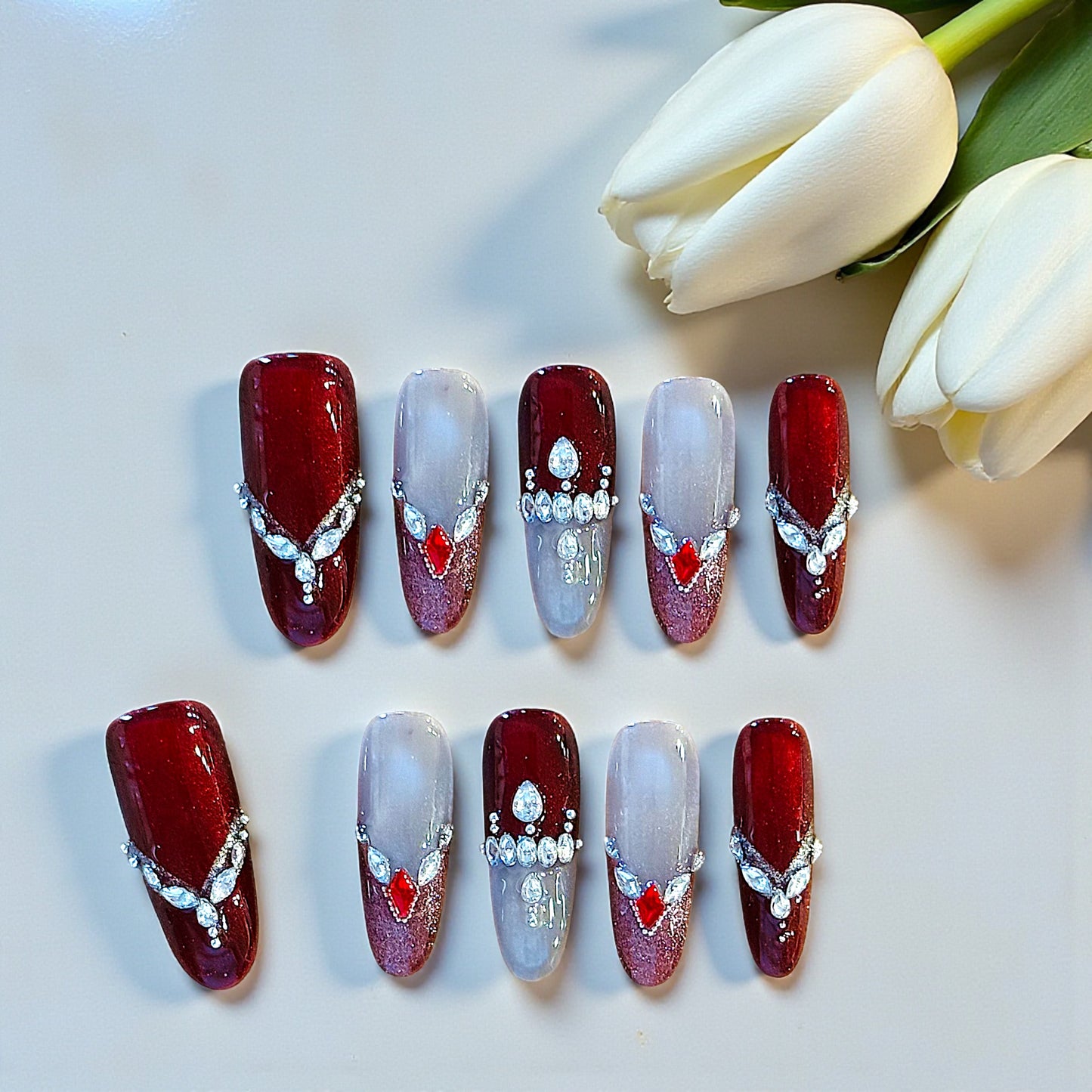 Decorative nail art with red and white designs on a light background with tulips.