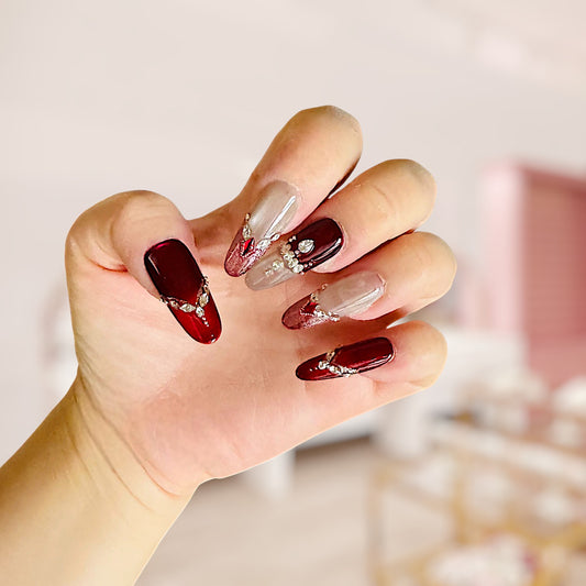 Hand with burgundy and clear nail polish featuring rhinestones against a blurred background