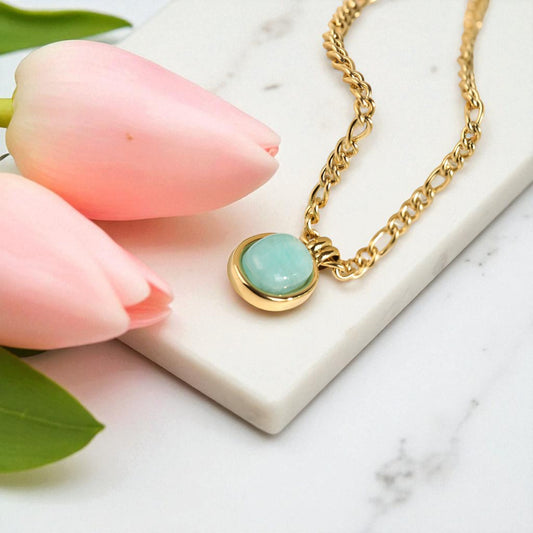 Gold necklace with a turquoise pendant held by pink tulips on a marble surface