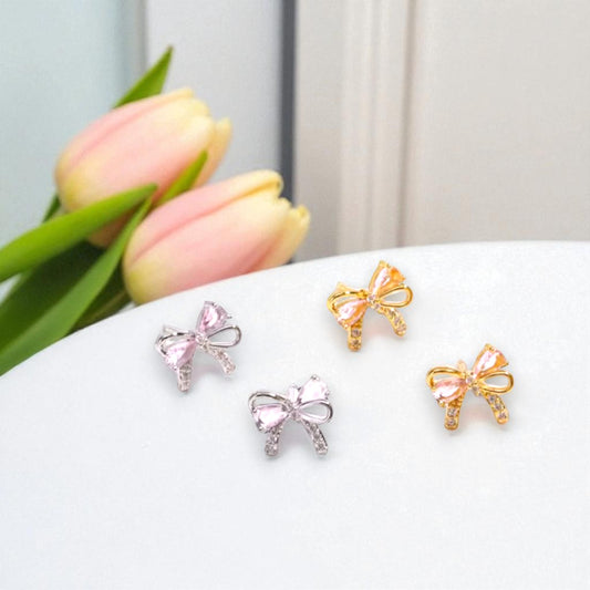 Bow-shaped earrings in gold and silver on a white surface with pink tulips in the background.
