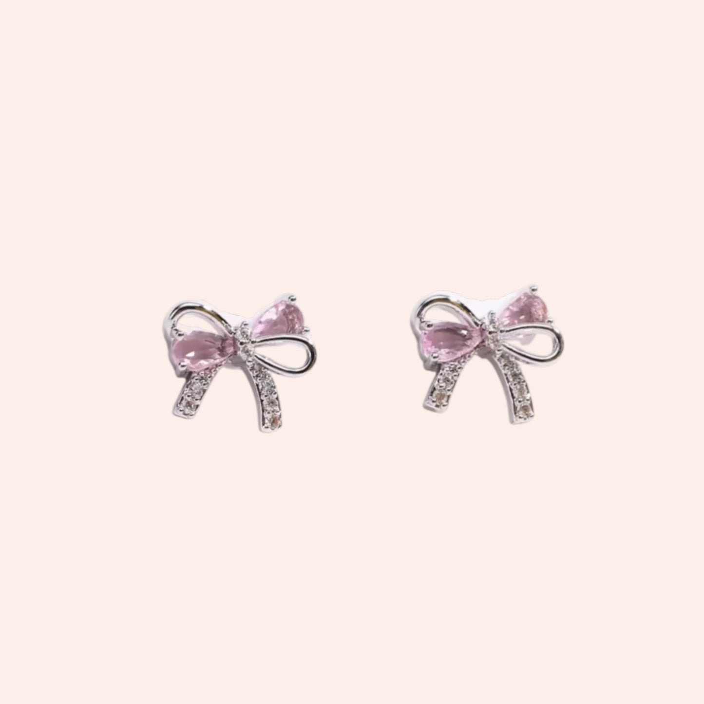 Pink bow-shaped earrings on a light pink background